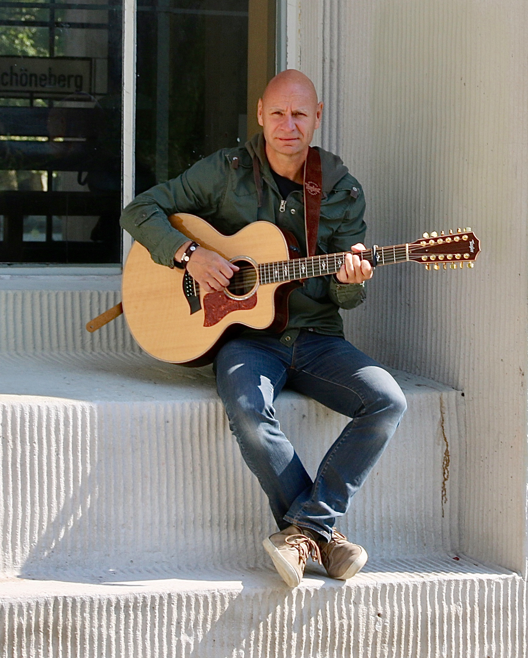 Der Solo-Künstler Randy sitzt auf einer weißen Treppe. Dabei sielt er auf seiner Akkustikgitarre.
